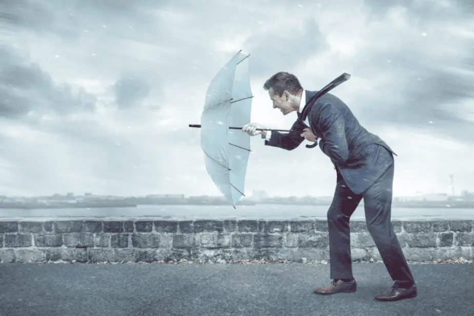 Business man with umbrella facing strong winds